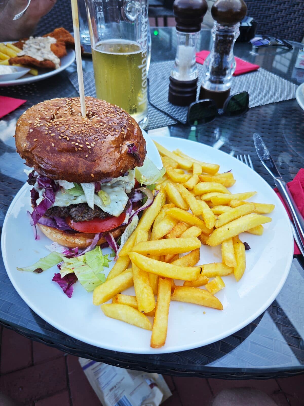 Hausgemachter Burger mit Sesambrötchen, Rindfleisch-Patty, Spiegelei, Tomate und Salat, dazu knusprige Pommes