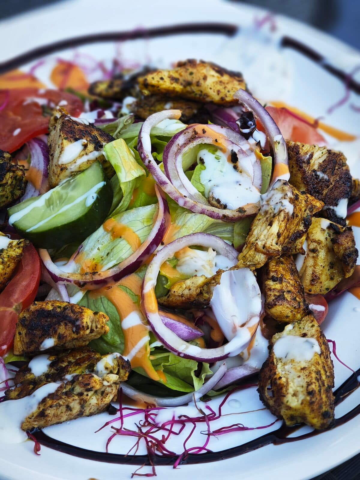 Bunter Blattsalat mit gegrillten, marinierten Hähnchenstreifen, Gurke, Tomate, roten Zwiebeln und zweierlei Dressing